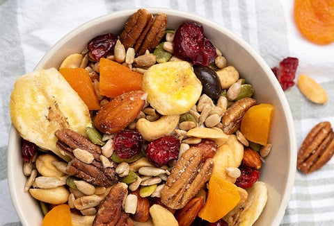 Nuts, bananas, apricots, and seeds mixed into trail mix in a white bowl.