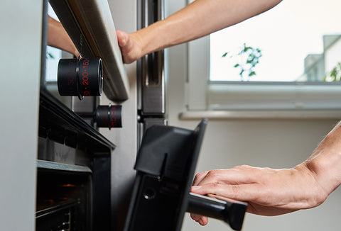 Two hands opening a black and silver oven.