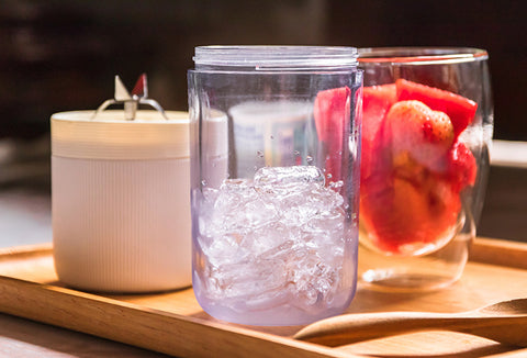 A clear blender bottle with ice, preparing for blending. A cup with berries is behind it.