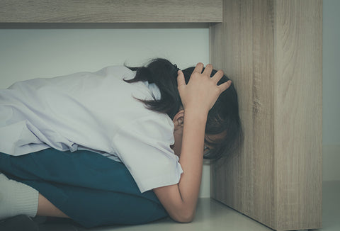 A girl hiding under a table to protect herself during an earthquake.