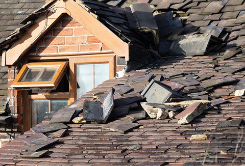 A roof of a home covered in broken shingles and debris caused by a hurricane.