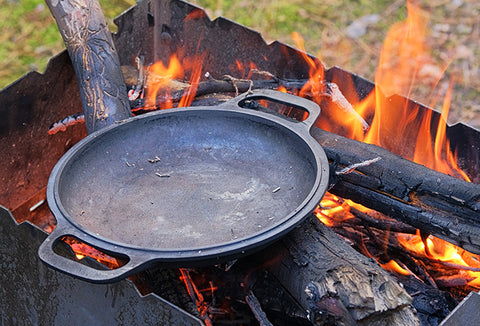 A cast iron skillet sitting on a bed of flames in a fire pit.