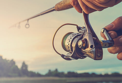 A man casting his fishing line into a lake with a sunset in the background.