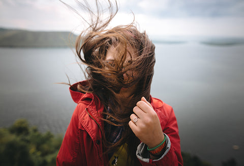 A woman in a red coat whose face is covered by her wind-blown hair.