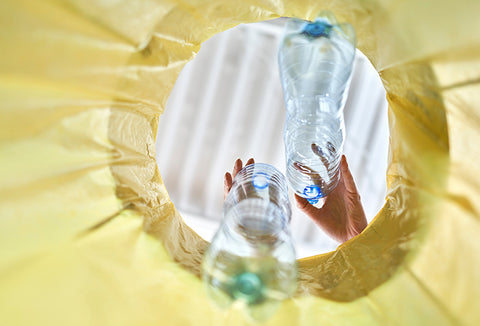 A yellow poncho lining a garbage can that people are throwing plastic bottles into.