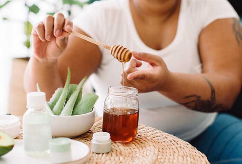 A woman applying honey to fingers to treat burns. Aloe plant and jar of honey nearby.