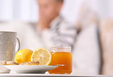 A plate with lemon and herbs next to a jar of honey. People sit on a couch in the background.