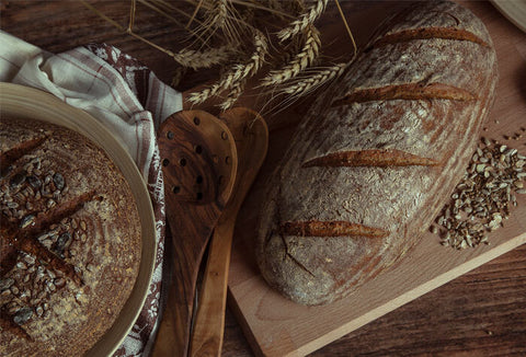 Two cracked loaves of artisan bread on wooden cutting boards.