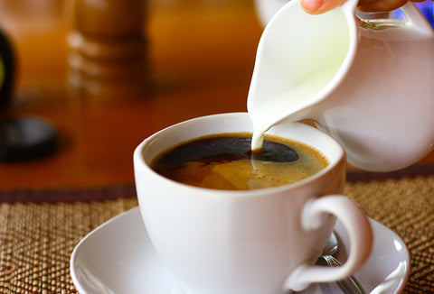 Someone pouring coffee creamer into a cup of coffee.