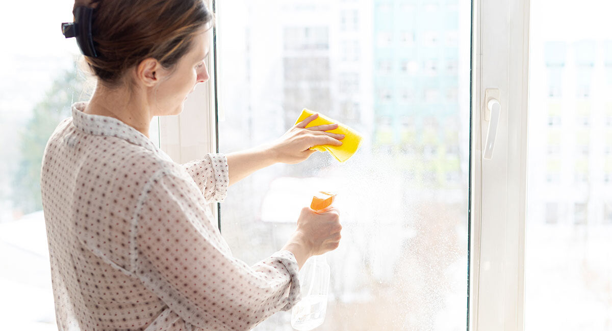 woman using vinegar to clean a window
