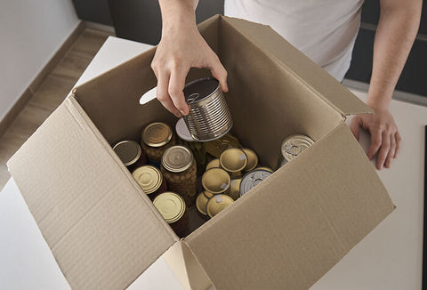 A person pulling canned food out of a cardboard box.