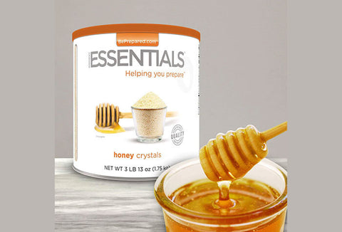 Emergency Essentials Honey Crystals #10 Can next to a bowl of honey with a honey dipper.