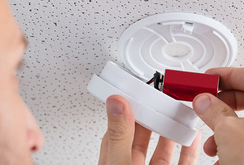 A man changing the batteries in a smoke detector. 