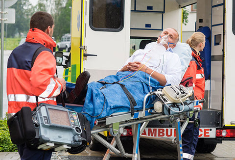 Man on an ambulance stretcher wearing an oxygen mask being pulled by two medics.