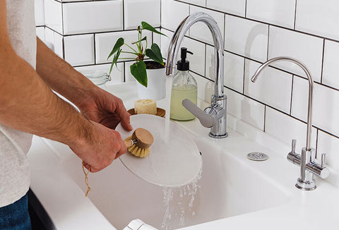 A person washing a white dish in a white sink, water coming from a silver faucet.
