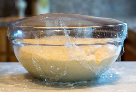 Dough in a glass bowl covered in plastic wrap.