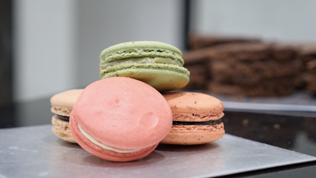 A pile of green, pink, and brown macarons on a gray table