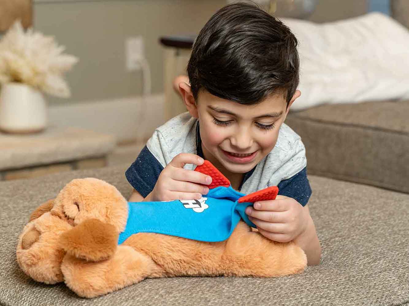 Young boy laying down and playing with his Snuggle Puppy HERO toy