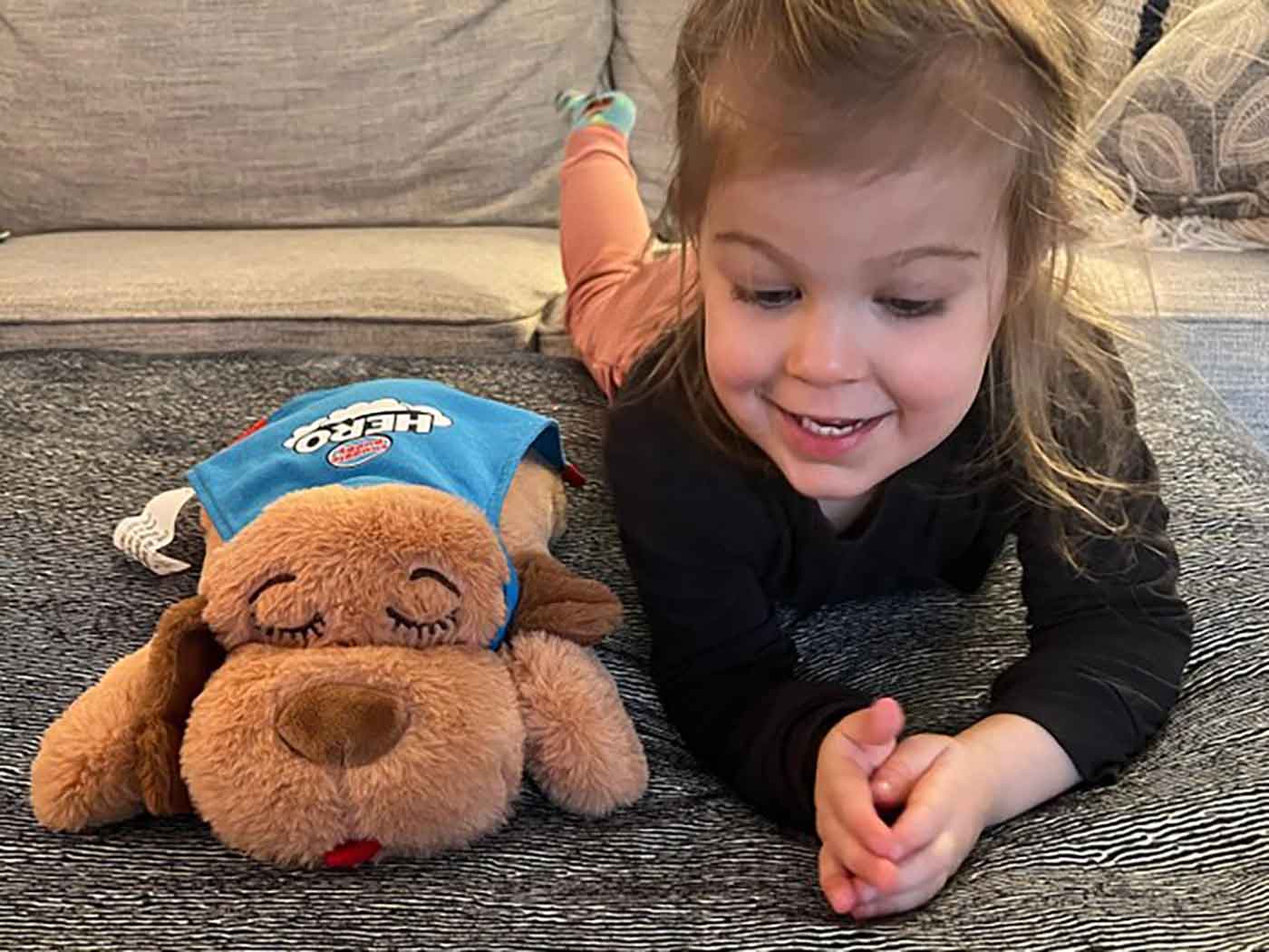 Young girl laying down and playing with her Snuggle Puppy HERO toy