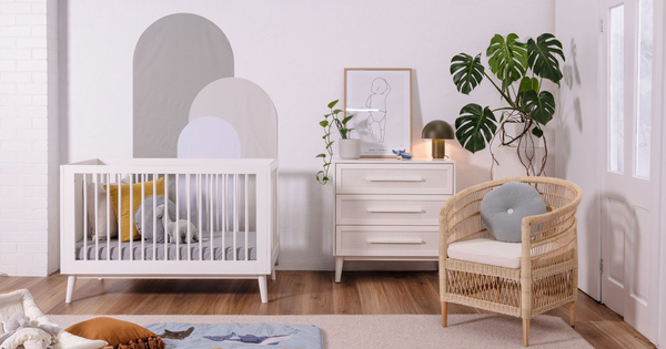 The Kaya cot and chest in white styled in a neutral, inviting nursery with soft blues and greys, a soft chair, plant and some toys scattered throughout.