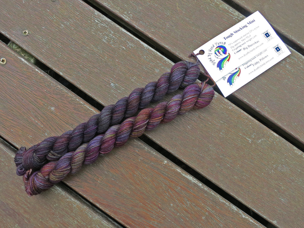 Two dark variegated mini skeins of yarn with white labels lie on a brown wooden background.
