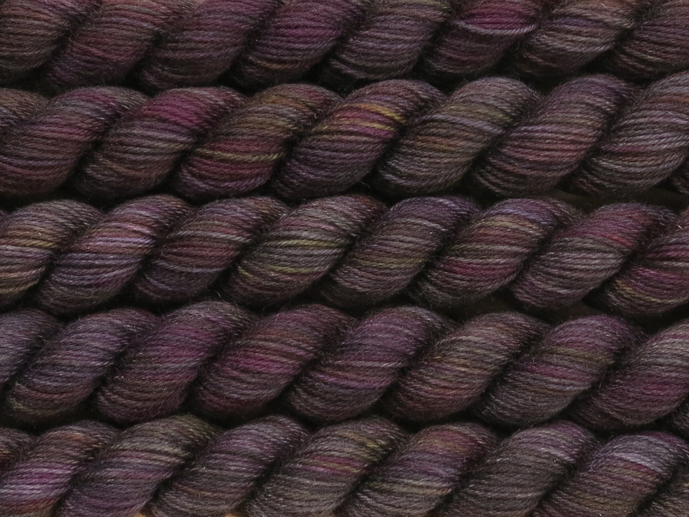 Multiple variegated mini skeins of yarn in black with undertones of pink, purple, orange and yellow lying vertically on the screen.