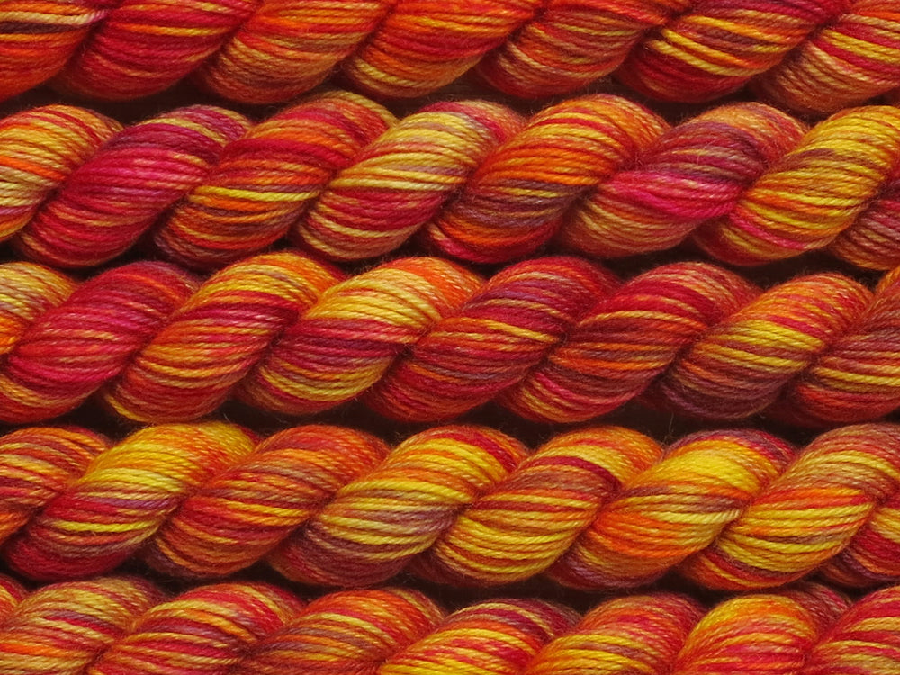 Multiple variegated mini skeins of yarn in yellow with undertones of pink, purple, orange and yellow lying vertically on the screen.