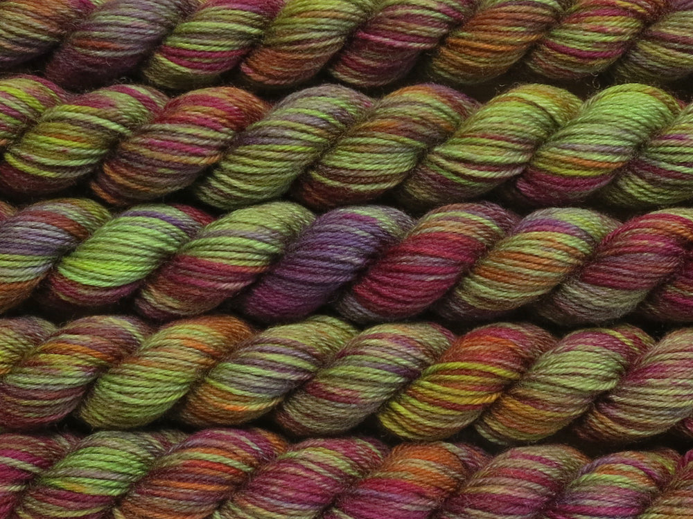 Multiple variegated mini skeins of yarn in green with undertones of pink, purple, orange and yellow lying vertically on the screen.