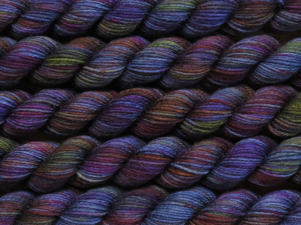 Multiple variegated mini skeins of yarn in navy blue with undertones of pink, purple, orange and yellow lying vertically on the screen.