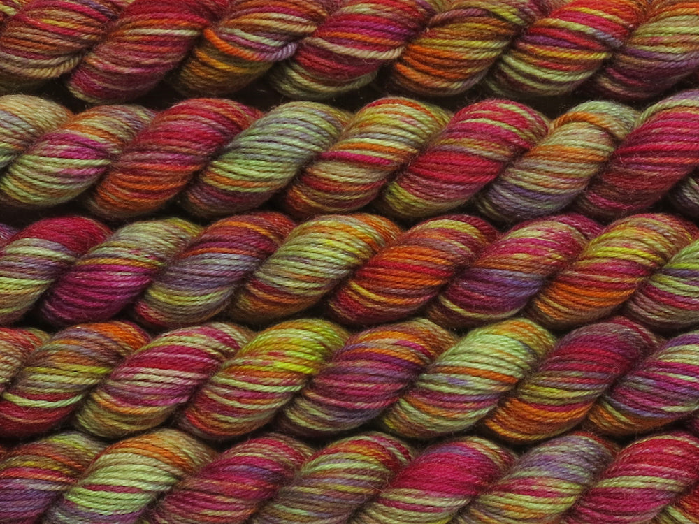 Multiple variegated mini skeins of yarn in light green with undertones of pink, purple, orange and yellow lying vertically on the screen.
