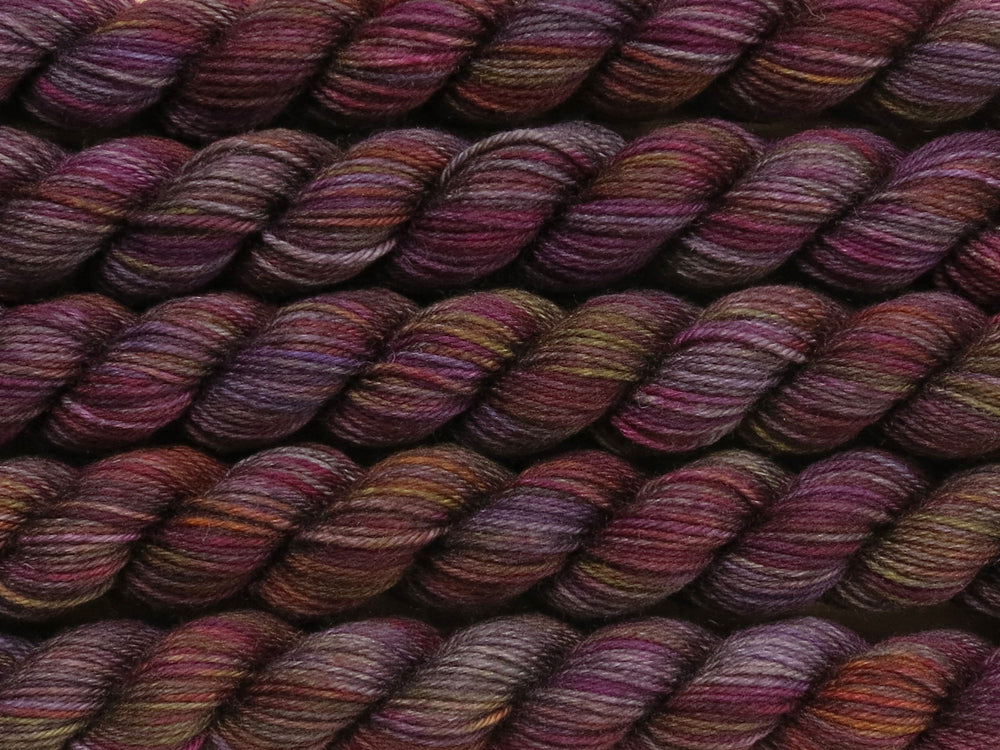 Multiple variegated mini skeins of yarn in charcoal grey with undertones of pink, purple, orange and yellow lying vertically on the screen.