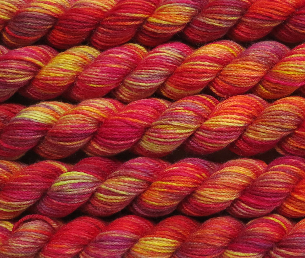 Multiple variegated mini skeins of yarn in light yellow with undertones of pink, purple, orange and yellow lying vertically on the screen.