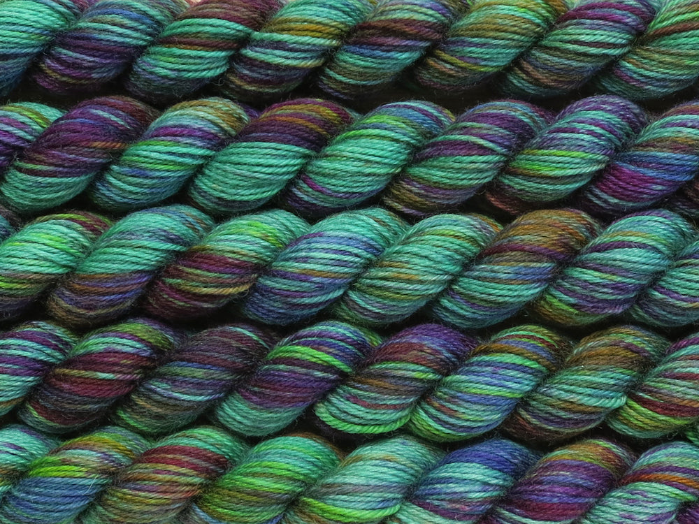 Multiple variegated mini skeins of yarn in teal with undertones of pink, purple, orange and yellow lying vertically on the screen.