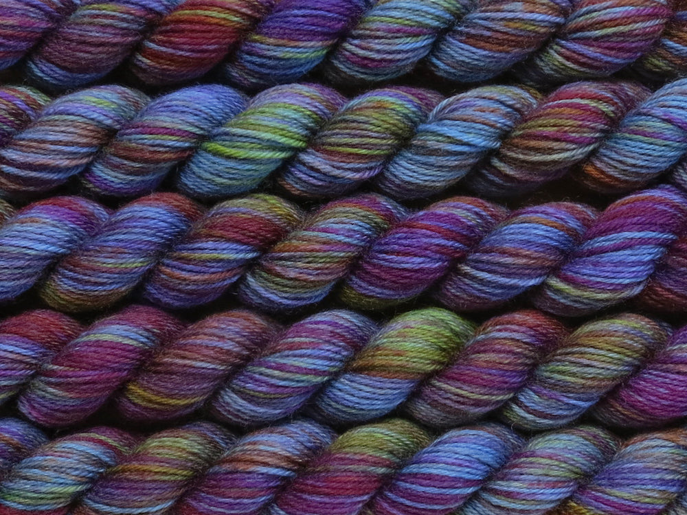 Multiple variegated mini skeins of yarn in blue with undertones of pink, purple, orange and yellow lying vertically on the screen.