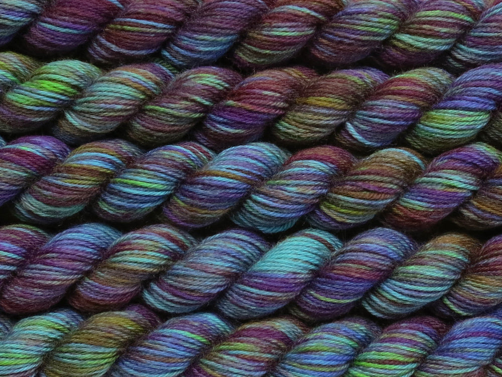 Multiple variegated mini skeins of yarn in blue-green with undertones of pink, purple, orange and yellow lying vertically on the screen.