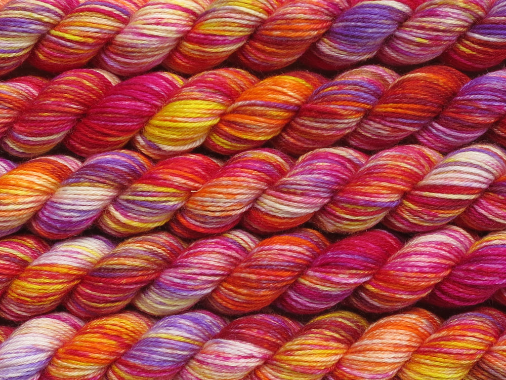 Multiple variegated mini skeins of yarn in variegated white, pink, purple, orange and yellow lying vertically on the screen.