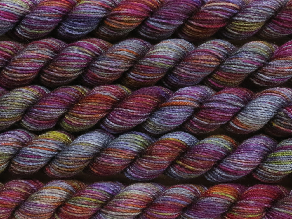 Multiple variegated mini skeins of yarn in medium grey with undertones of pink, purple, orange and yellow lying vertically on the screen.