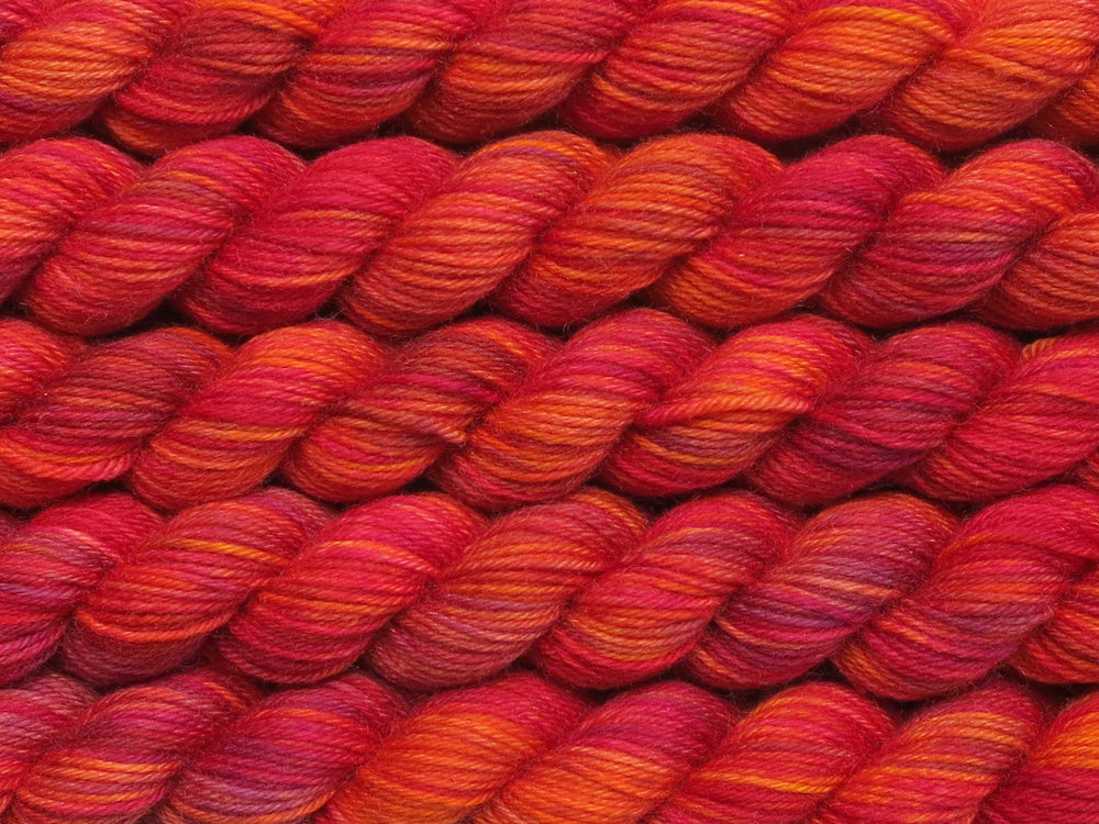 Multiple variegated mini skeins of yarn in orange with undertones of pink, purple, orange and yellow lying vertically on the screen.