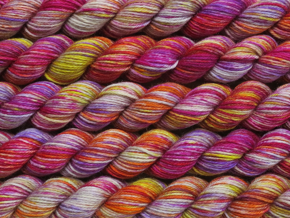 Multiple variegated mini skeins of yarn in pale grey with undertones of pink, purple, orange and yellow lying vertically on the screen.
