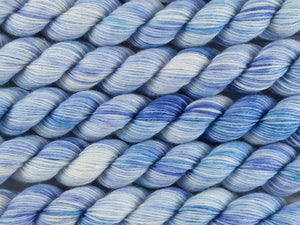 A close up of variegated white with blues and teal mini skeins of superwash merino and nylon 4ply fingering sock yarn arranged horizontally (Katabatic Winds on Tough Stocking Mini)