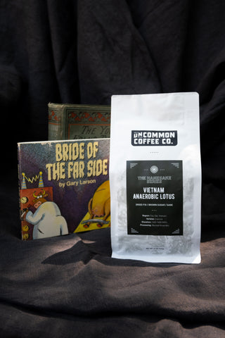 a bright white coffee bag with a dark matte navy label that reads "Vietnam Anaerobic Lotus".  The bag is set slightly in front of a Far Side comic and the background is a dark fabric drape.