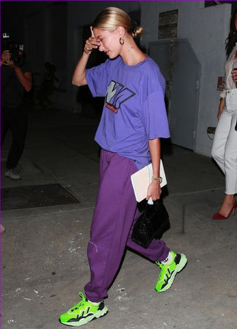 Young woman wearing a Y2K outfit in purple - loose graphic t-shirt, joggers and electric green sneakers.