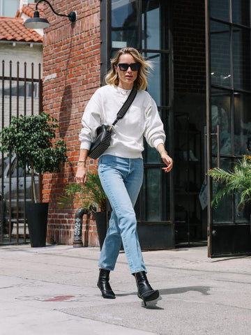 Classy woman wearing a white sweatshirt, blue jeans and black boots, walking down the street.