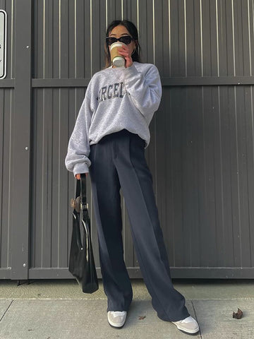Stylish woman wearing a grey sweatshirt and grey trousers, drinking coffee.