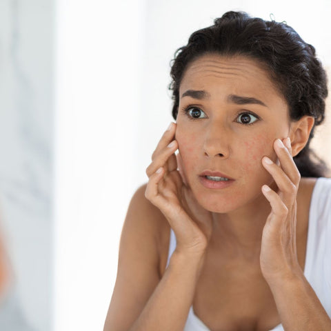 Concerned woman looks at irritated skin in mirror