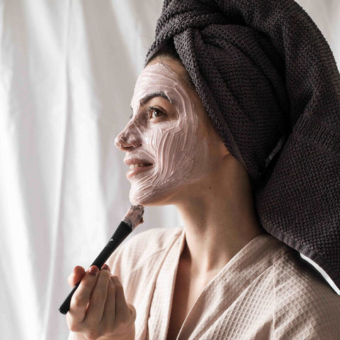 woman applying face masque with brush in bathrobe and towel