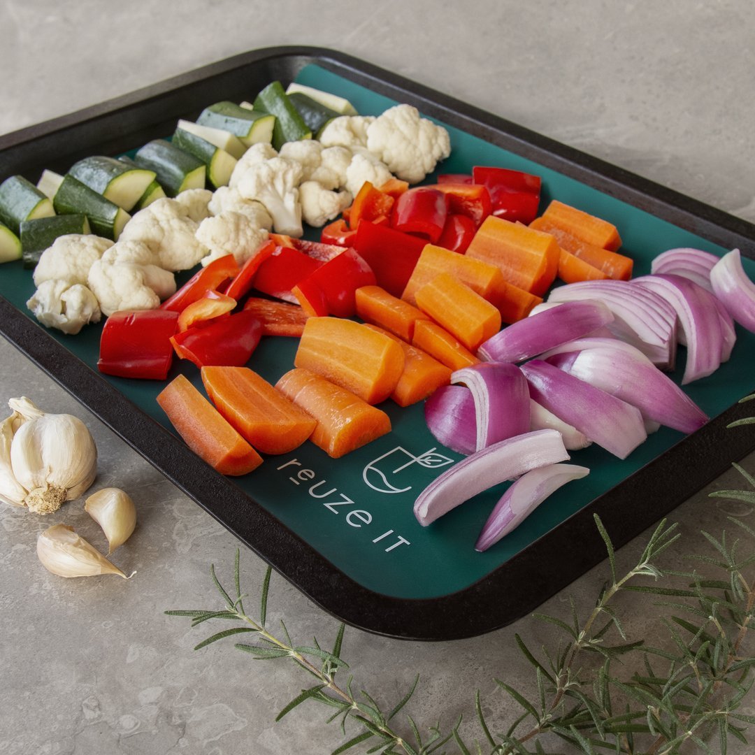 A silicone baking mat on a baking tray filled with cut up vegetables.
