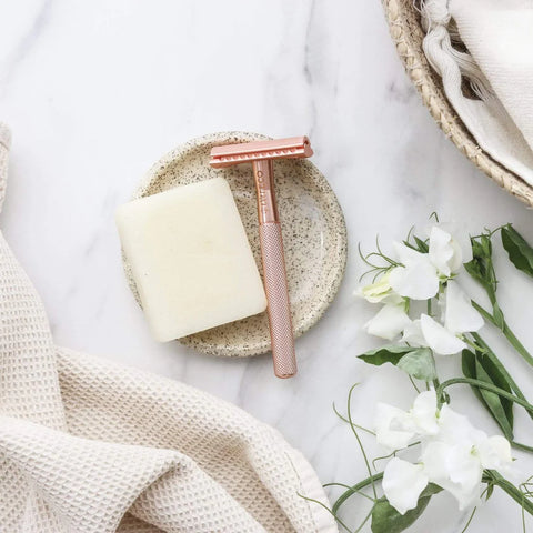 a rose gold safety razor with a block of soap on a tray surrounded by flowers