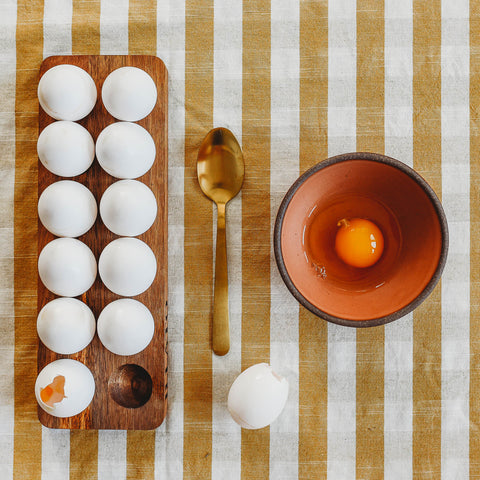 A wooden tray of eggs and a bowl with a raw egg inside to make hollow cascarones.