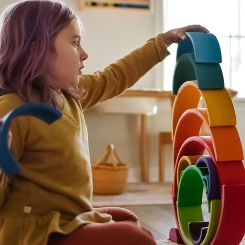 child with purple hair stacking wooden rainbow arches